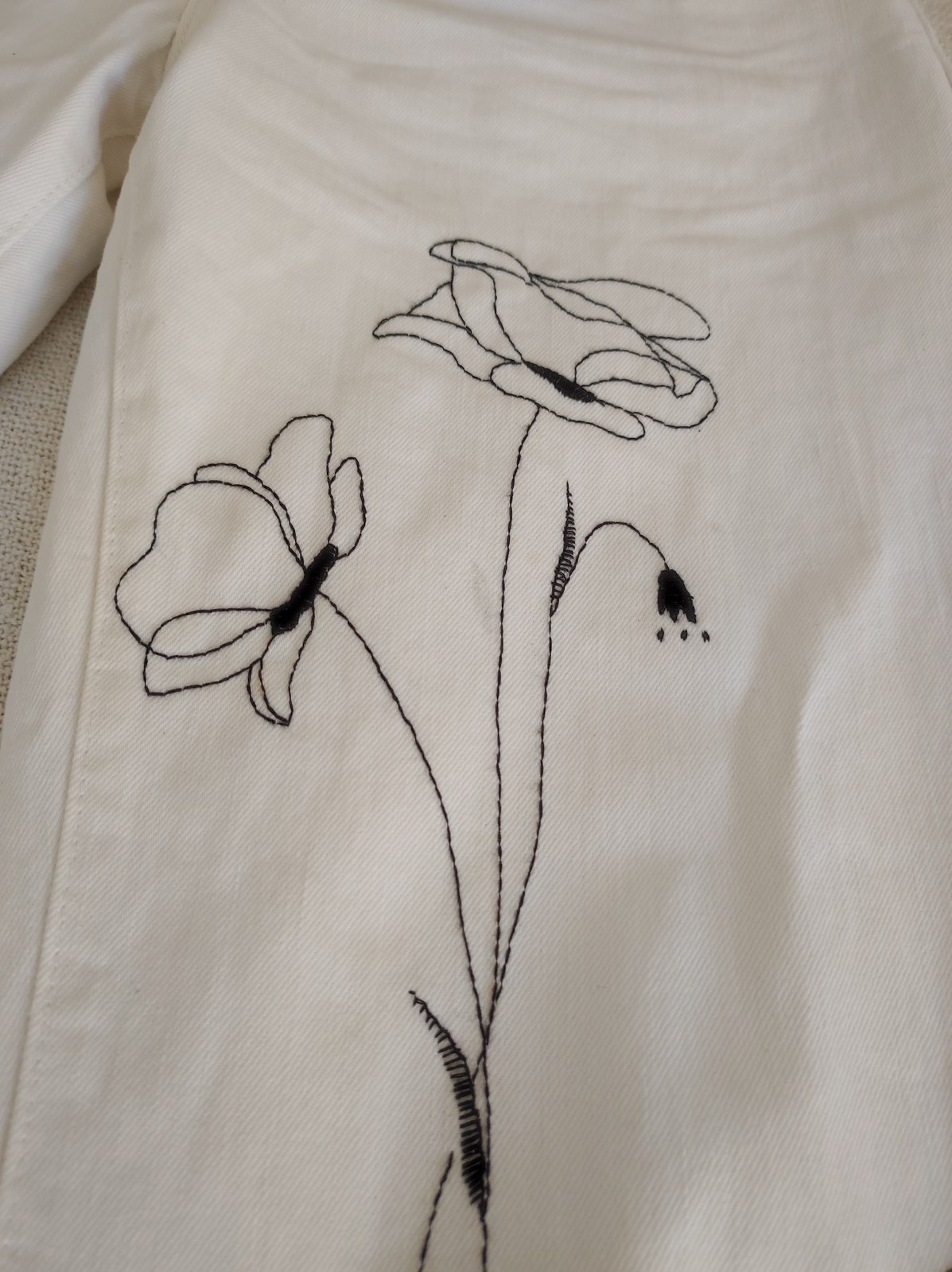 Close up of black botanical embroidery on white denim