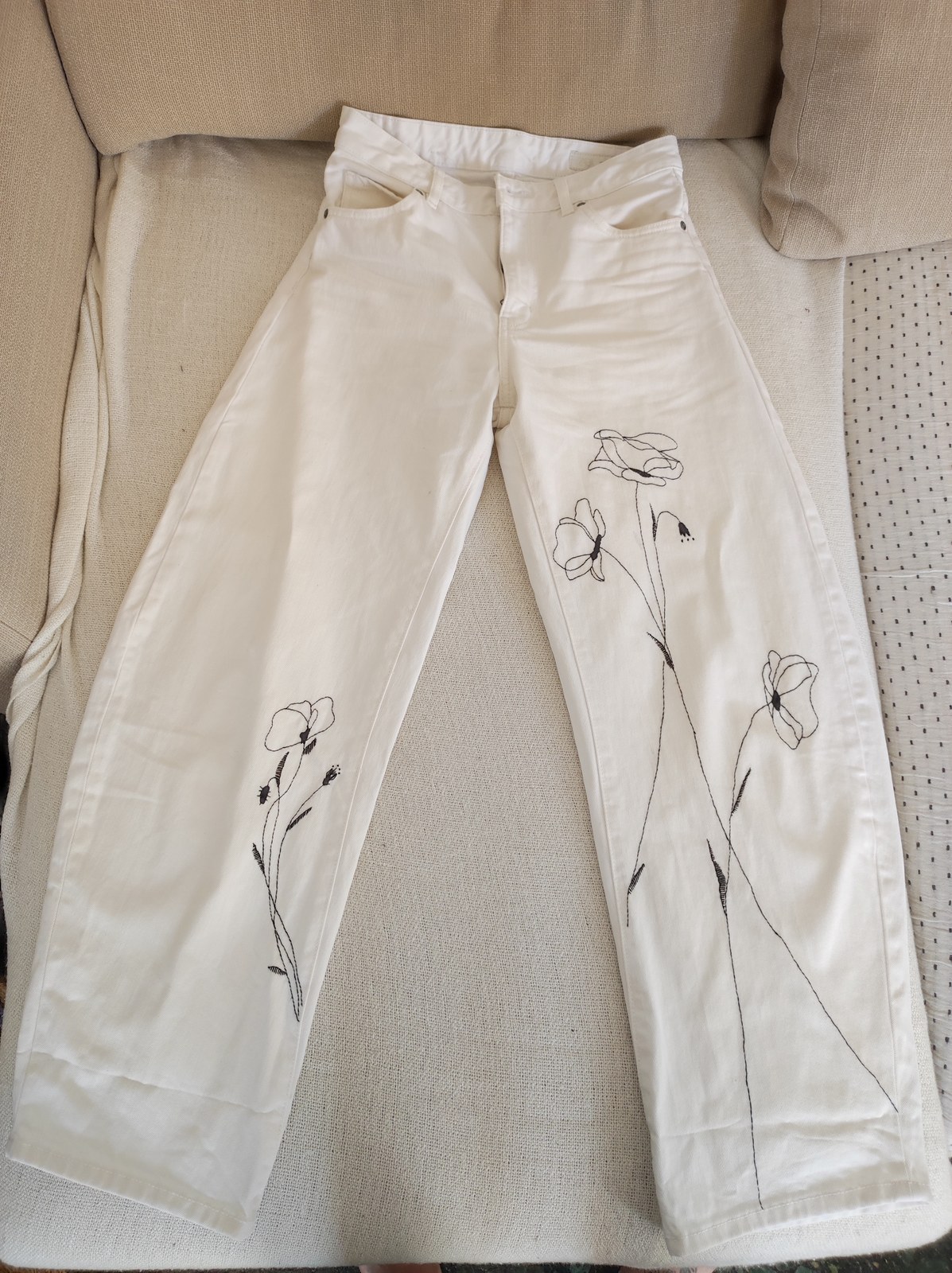 Full view of white denim jeans with black botanical embroidery
